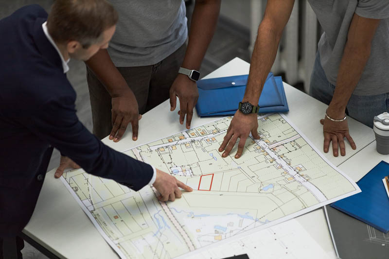 FABCO Commercial property experts reviewing architectural blueprint on office table, foreman pointing at building plan